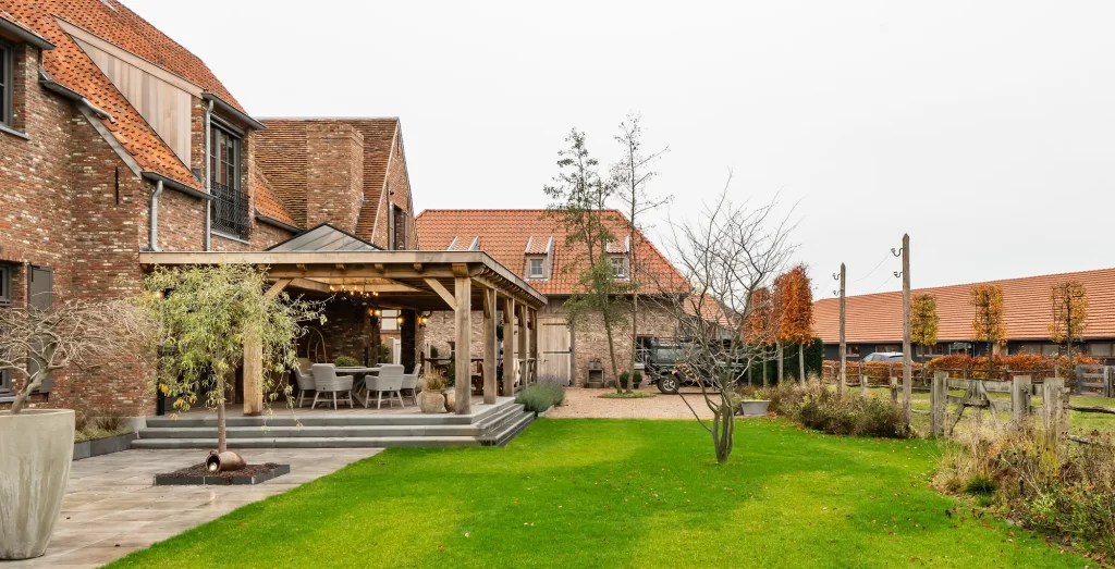 Breed zicht over gazon op een bakstenen woning met eikenhouten overkapping.
