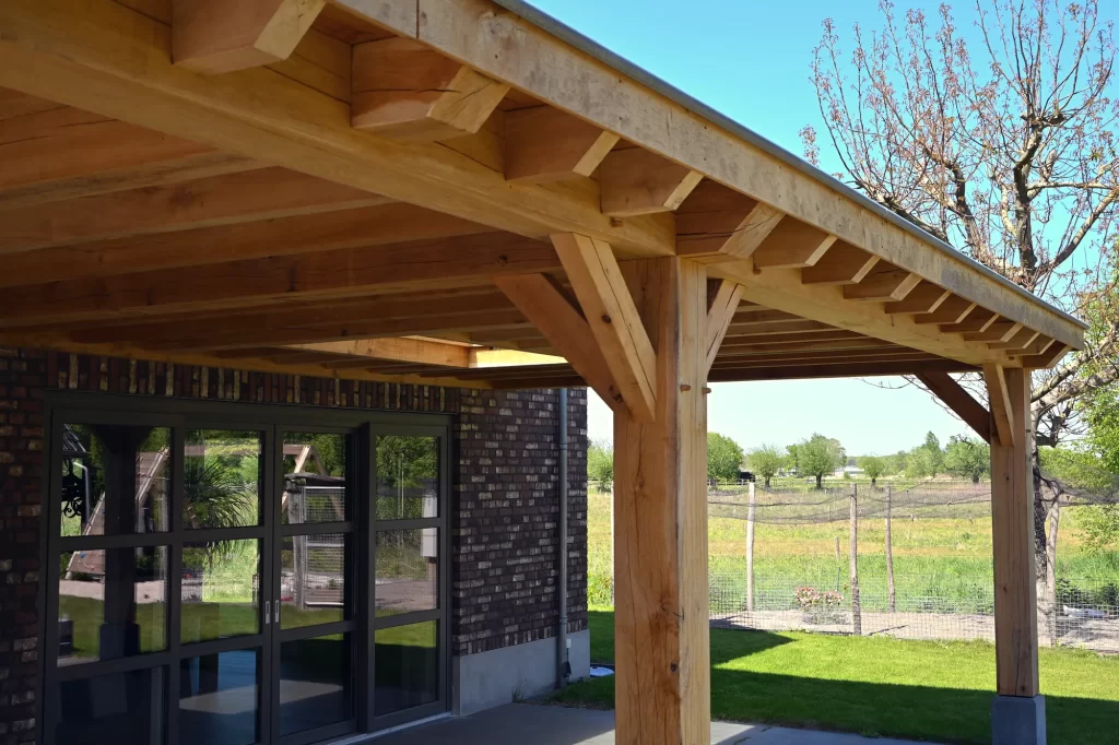 Eikenhouten terrasoverkapping met staanders en schoren voor een glazen gevel aan het gazon.
